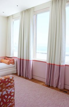 a living room filled with furniture and large windows covered in curtains next to a pink rug