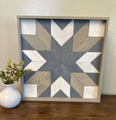 a white vase sitting on top of a wooden table next to a framed artwork piece