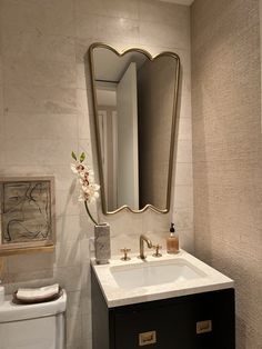 a white toilet sitting next to a bathroom sink under a large golden mirror above it