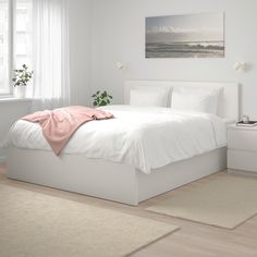 a bedroom with white walls and flooring has a pink blanket on the headboard