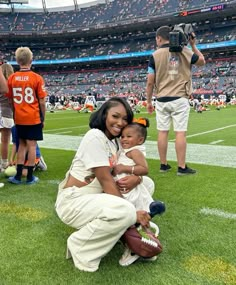 a woman kneeling down with a baby on her lap in front of a football field