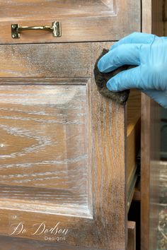 a person in blue gloves and rubber gloves cleaning an old wooden cabinet with a rag