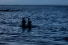 two people standing in the ocean at night with their backs turned to the camera,