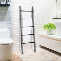 a white toilet sitting next to a bath tub in a bathroom under a ladder towel rack