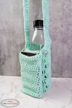 a crocheted bag with a bottle in it on a marble countertop next to a gray wall