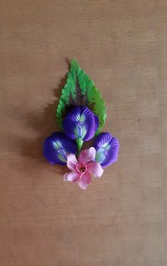 a purple flower with green leaves and pink flowers on a wooden surface, in front of a brown background