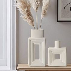 two white vases sitting on top of a wooden table next to a framed painting