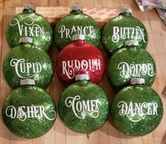 six green christmas ornaments with white lettering on them and one red ornament in the middle