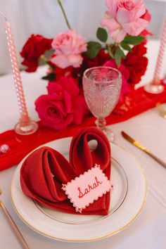 a place setting with red napkins and pink roses in the center, along with candles