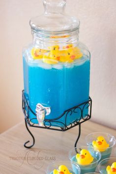 blue liquid with yellow rubber ducks in it and four small plastic cups on the table