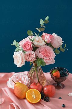 a vase filled with flowers and fruit on top of a pink table cloth next to an orange slice