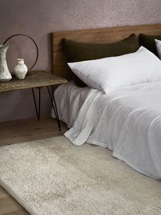 a bed with white linens and pillows in a small room next to a table