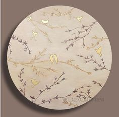 a wooden plate with birds and branches painted on the front in gold, white and grey