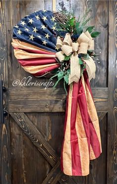 an american flag wreath hanging on the side of a barn door with greenery and ribbons