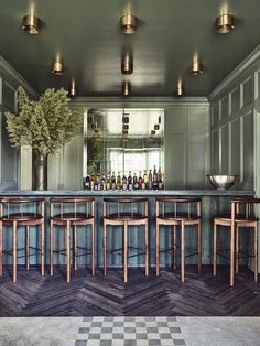 a bar with several stools and bottles on the back wall, in front of a checkerboard floor