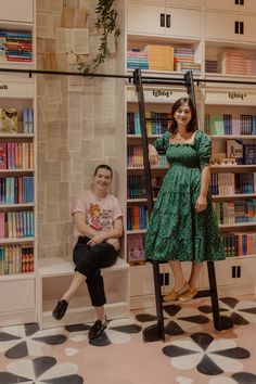 a man and woman posing for a photo in front of a bookshelf with shelves full of books