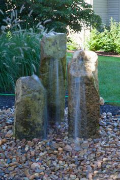 three stone water fountains sitting in the middle of a gravel area next to a house