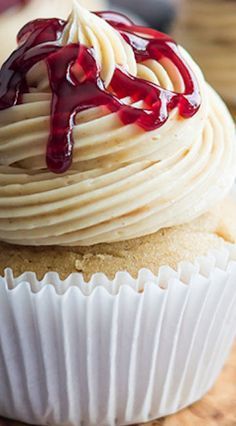 a cupcake with white frosting and drizzled red sauce on top