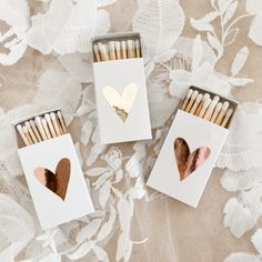 three matches with heart cutouts in them on a lace covered tablecloth, one is white and the other is gold