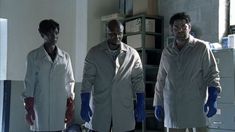 three men in lab coats standing next to each other with blue gloves on their hands