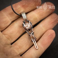 a hand holding a wire wrapped pendant with scissors