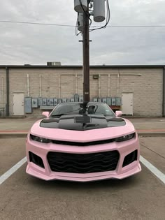 a pink sports car parked in a parking lot next to a pole with a basketball hoop on it