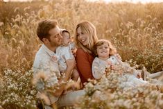 a man, woman and two children are sitting in a field with tall grass at sunset