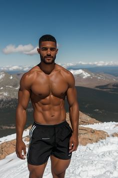 a shirtless man standing on top of a snow covered mountain with his hands in his pockets