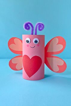 a toilet paper roll with a heart and two antennae on it, sitting in front of a blue background