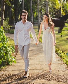 a man and woman walking down a path holding hands while the horse is in the background