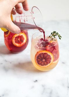 someone pouring wine into a glass filled with blood oranges and garnished with herbs