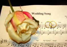 two wedding rings sitting on top of an old sheet of music with a rose in the middle