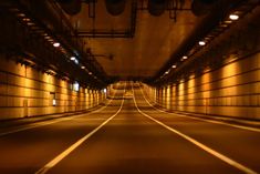 an empty tunnel with no cars on the road and lights at the end in the distance