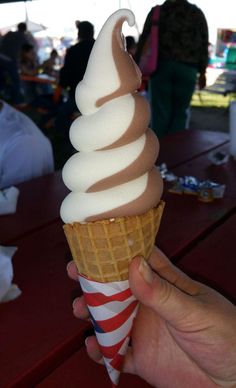 a hand holding an ice cream cone with chocolate and white icing on it at a picnic table