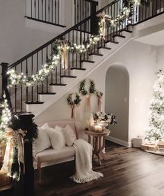 a living room filled with furniture and christmas lights on the staircases, along with garlanded trees