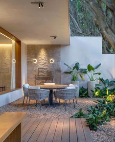 an outdoor dining area with wooden flooring and white walls, surrounded by greenery