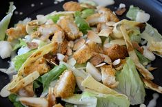 a salad with lettuce, chicken and almonds in a black bowl on a table