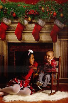 two young children sitting in front of a fireplace with stockings on the mantels