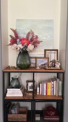 a vase with flowers on top of a book shelf filled with books and other items