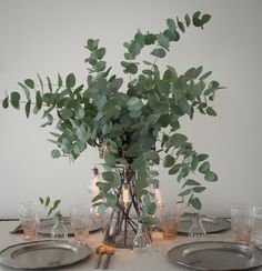 a table set with plates, silverware and a vase filled with greenery on it