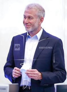 an older man in a suit is holding something up to his chest and looking at the camera