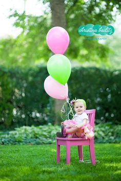 a baby sitting on a pink chair with some balloons in the air above her head