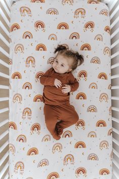 a baby laying in a crib with rainbows on it