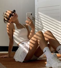 a woman sitting on the ground with her cell phone up to her ear and wearing sunglasses