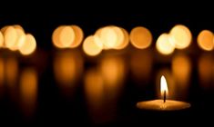 a lit candle sitting on top of a table next to many other small candles in the background