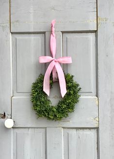 a pink bow hangs on the front door of an old white door with a wreath