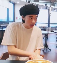 a young man sitting at a table with food in front of him and wearing a black hat