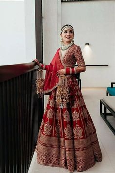 a woman in a red and gold bridal gown standing on a balcony with her arms out