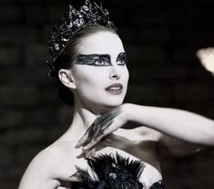 a woman with black makeup and feathers on her face is posing for the camera in front of a chandelier