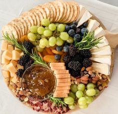 a platter with cheese, crackers, grapes, nuts and fruit on it